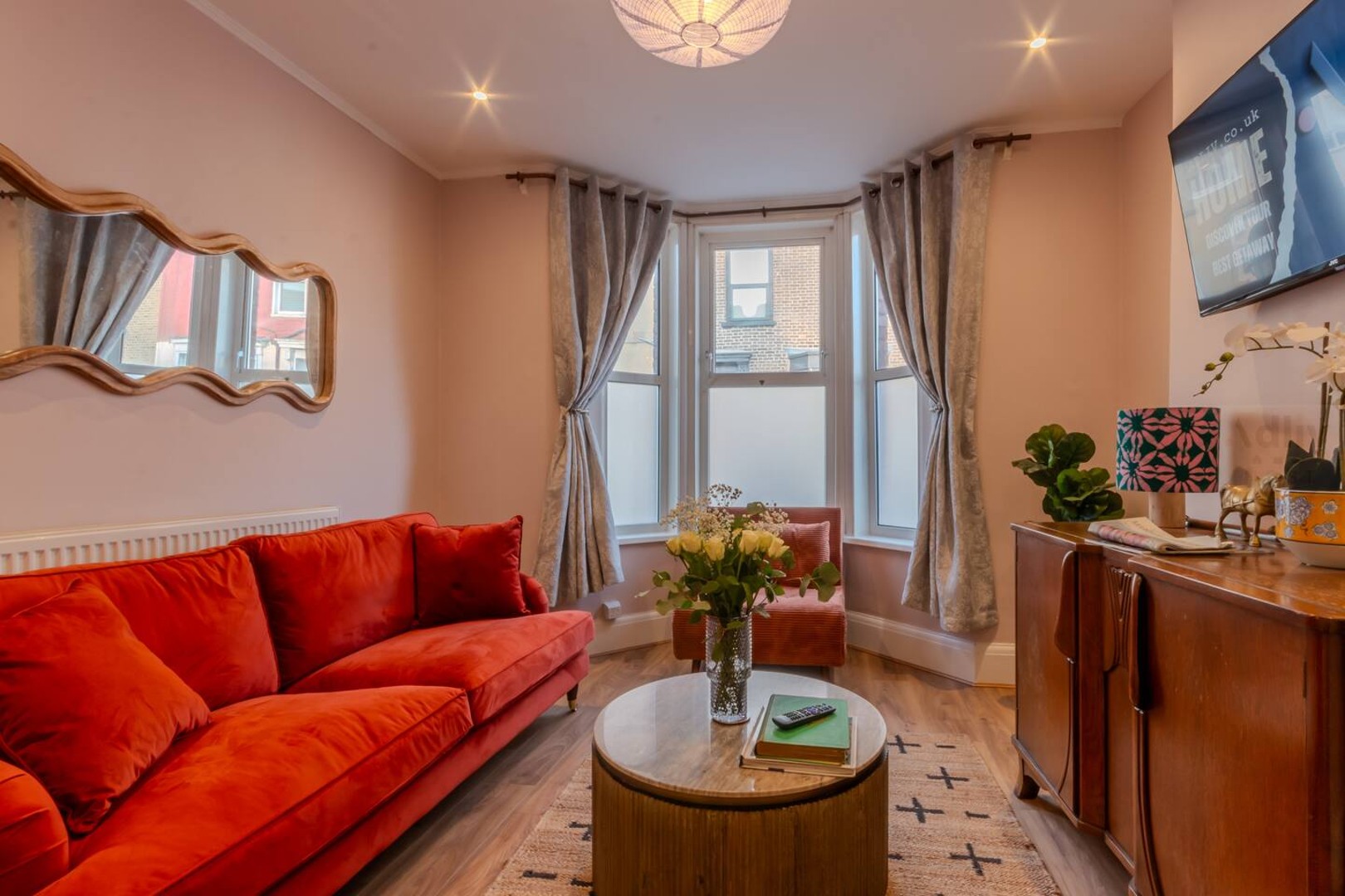Stylish lounge with a bold orange sofa, smart TV, and Netflix u2014 a cosy space to relax or work, filled with natural light from the bay window.