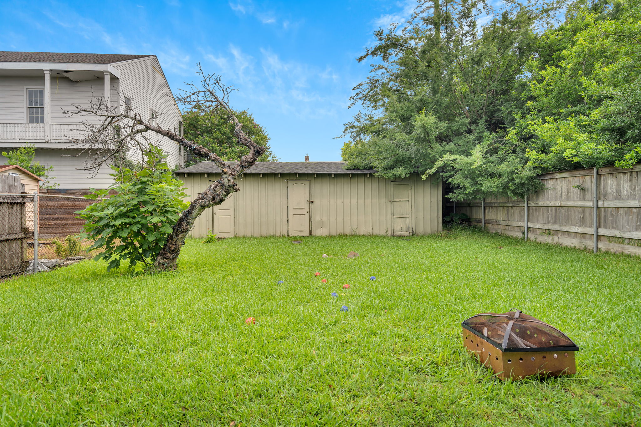 Large fenced yard with fire pit and shade tree.