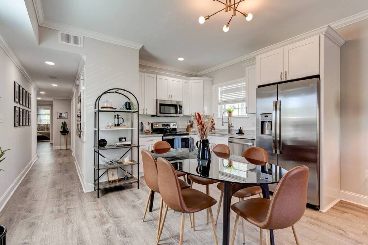 Modern kitchen and dining area featuring a sleek table that comfortably seats six, stainless steel appliances, and stylish open shelving for a touch of elegance.