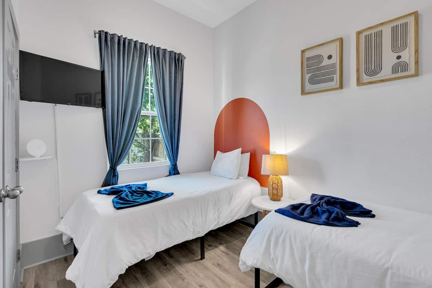 This vibrant twin room blends modern minimalism with a pop of color!  The bold orange arches, soft lighting, and cozy bedding make it a stylish yet inviting retreat.  Perfect for friends or family!