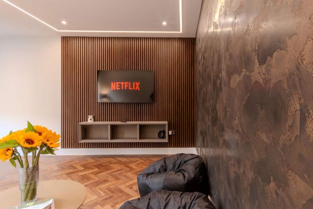 Luxury Smart TV Lounge with Ambient LightingnUnwind in a stylish open-plan living space featuring warm mood lighting, parquet flooring, ultra-fast Wi-Fi and a large Smart TV perfect for Netflix nights, long stays and city breaks.