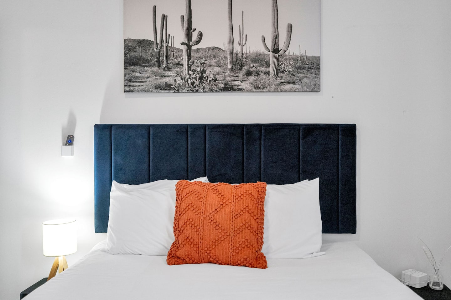 This chic and cozy bedroom features a velvet navy headboard, crisp white bedding, and a bold pop of burnt orange for a perfect blend of sophistication and warmth!