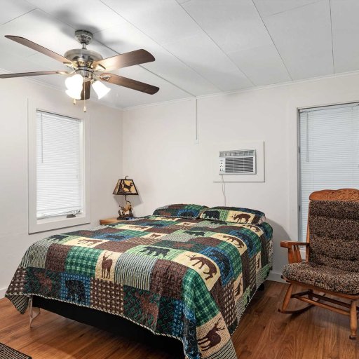 Bedroom 1 — Queen bed with ceiling fan, rocking chair, and window AC