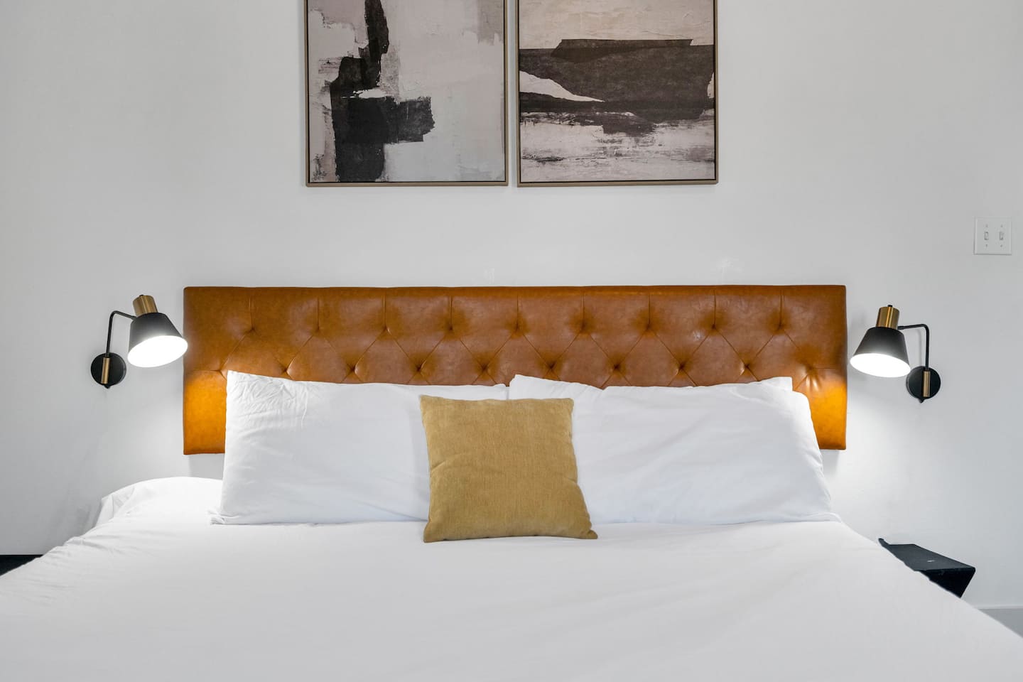 Experience luxury up close! This elegant bedroom features a sleek tufted leather headboard, modern wall sconces, and stylish abstract artwork, creating the perfect blend of comfort and sophistication.