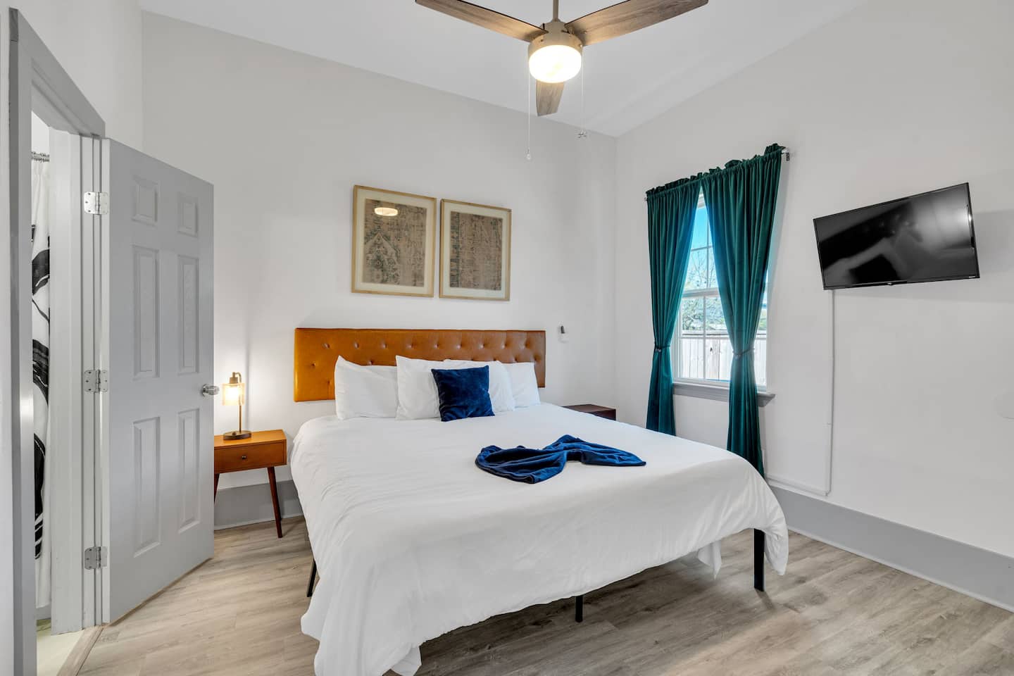 Relax in this cozy bedroom featuring a plush king-size bed, elegant decor, and rich emerald curtains. Enjoy a Smart TV, ceiling fan, and warm bedside lighting for ultimate comfort. Your perfect retreat awaits!