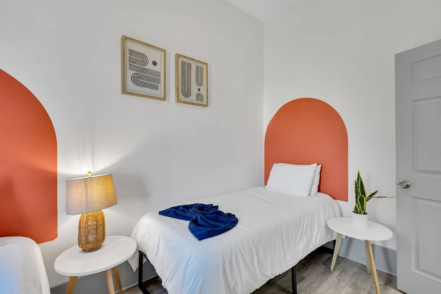 This bright and modern twin bedroom blends bold design with cozy charm! The eye-catching terracotta arches add warmth, while the sleek black-framed artwork and deep blue curtains create a striking contrast.